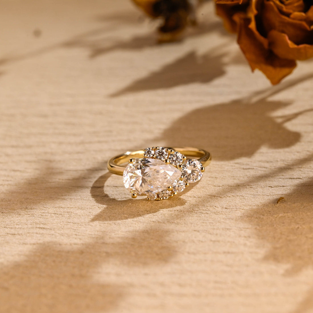 East west pear cut moissanite cluster engagement ring with a round stone at the point and graduated small round stones along the edges on a plain yellow gold band