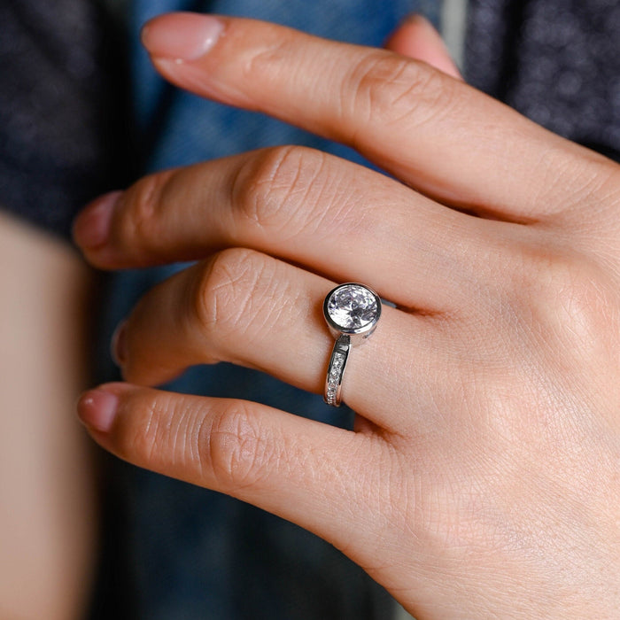 Round moissanite bezel set solitaire engagement ring with a smooth full bezel and a white gold band channel set with small round stones, view 2