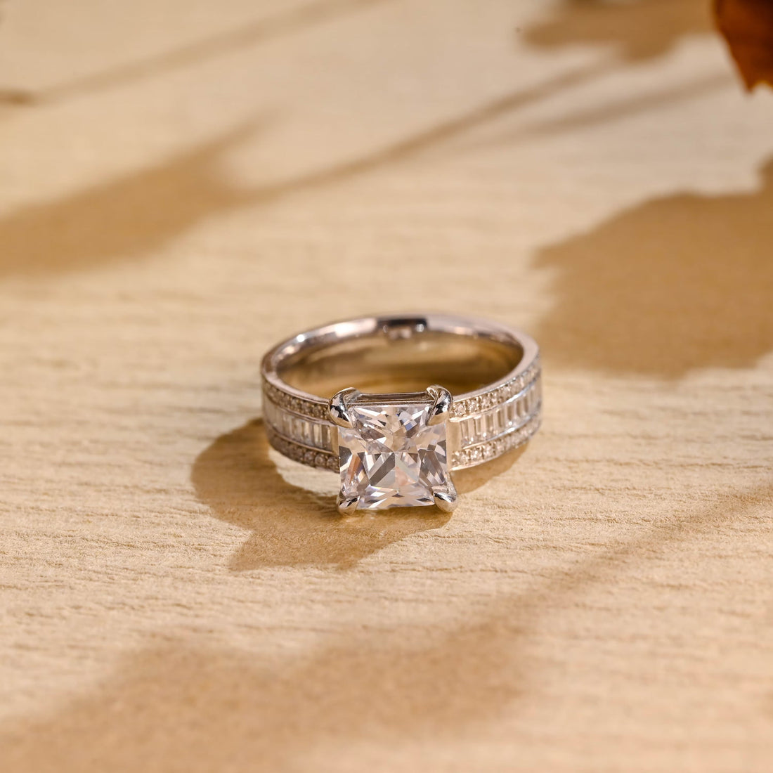 Princess cut moissanite solitaire engagement ring on a wide white gold band set with baguette and pave stones