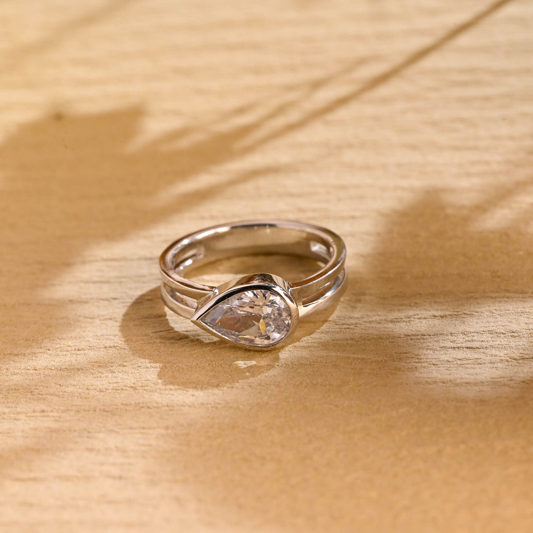 East west bezel set pear cut moissanite solitaire engagement ring on a polished white gold two strand double band