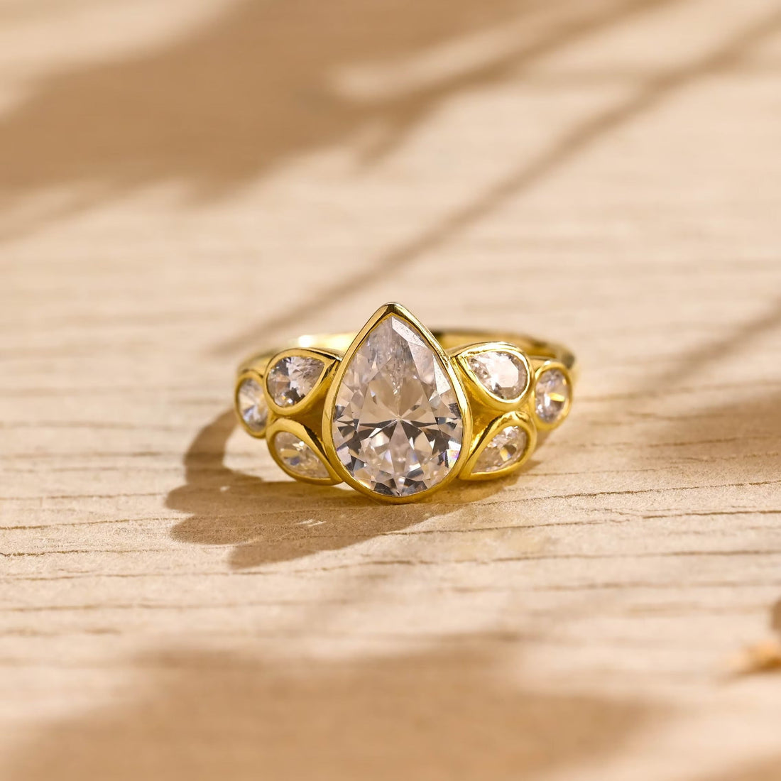 Bezel set pear cut moissanite cluster engagement ring with petal shaped bezel set pear and round side stones in yellow gold