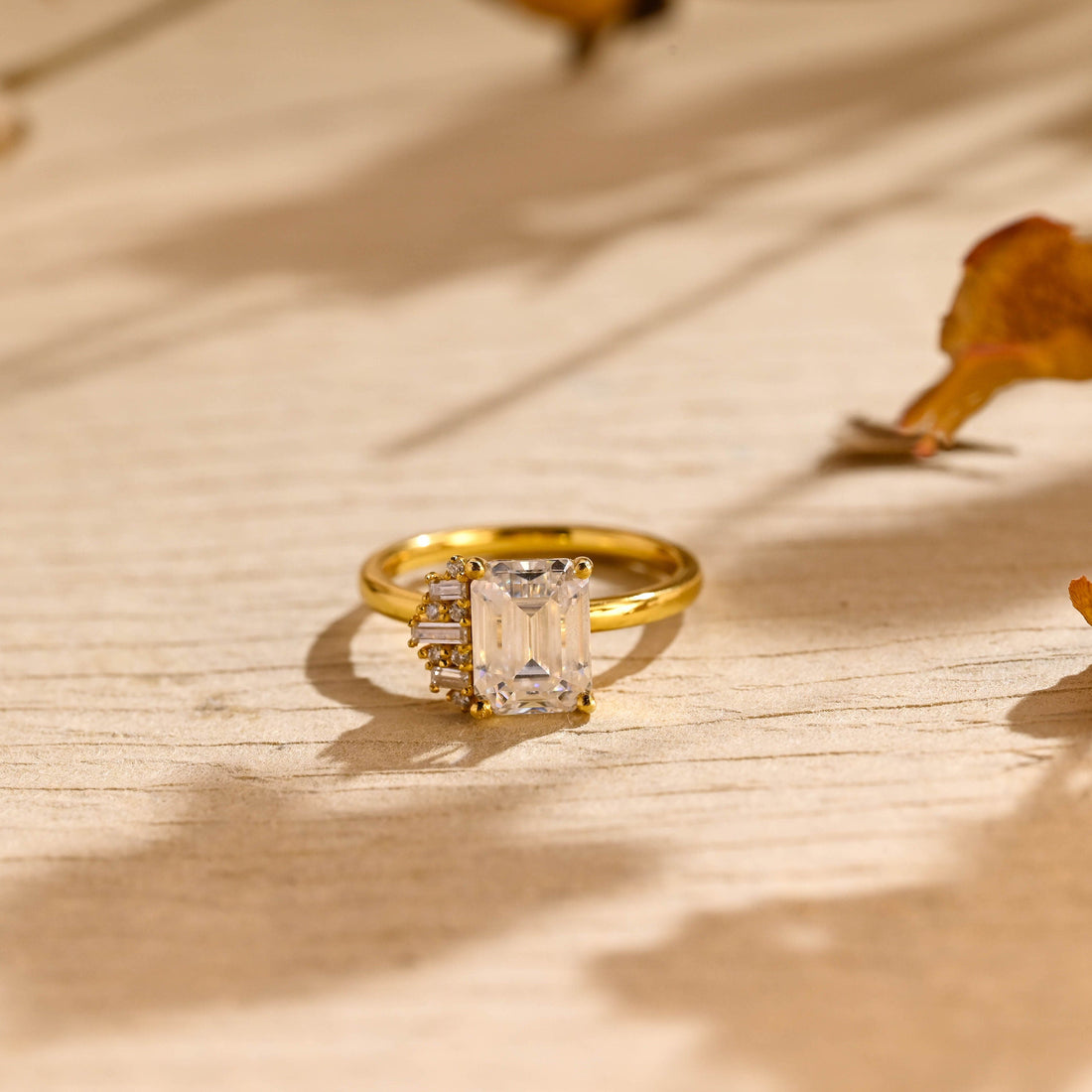 Emerald cut moissanite engagement ring with a one sided cluster of baguette and round stones on a plain yellow gold band