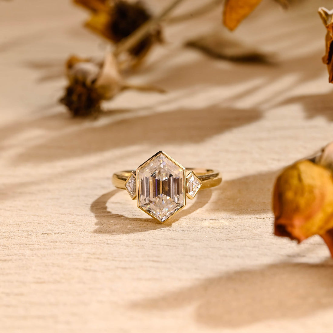 Bezel set hexagon cut moissanite three stone engagement ring with kite cut side stones in yellow gold