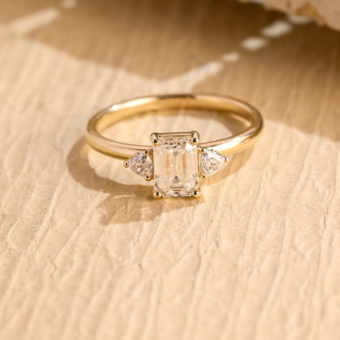 Emerald cut moissanite three stone engagement ring with a trillion cut stone on each side of a slim yellow gold band