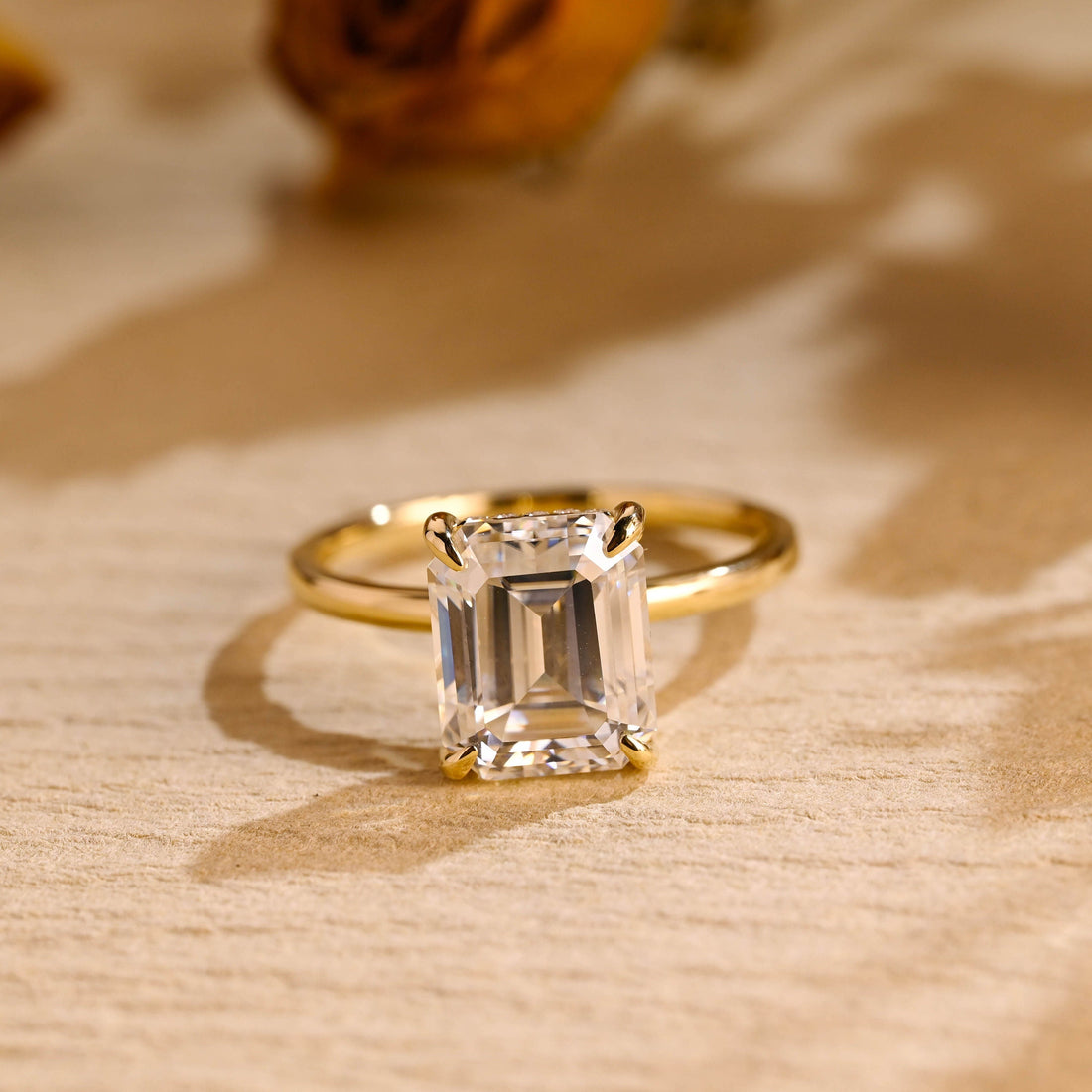 Emerald cut moissanite hidden halo solitaire engagement ring with four tapered claws on a plain slim polished yellow gold band
