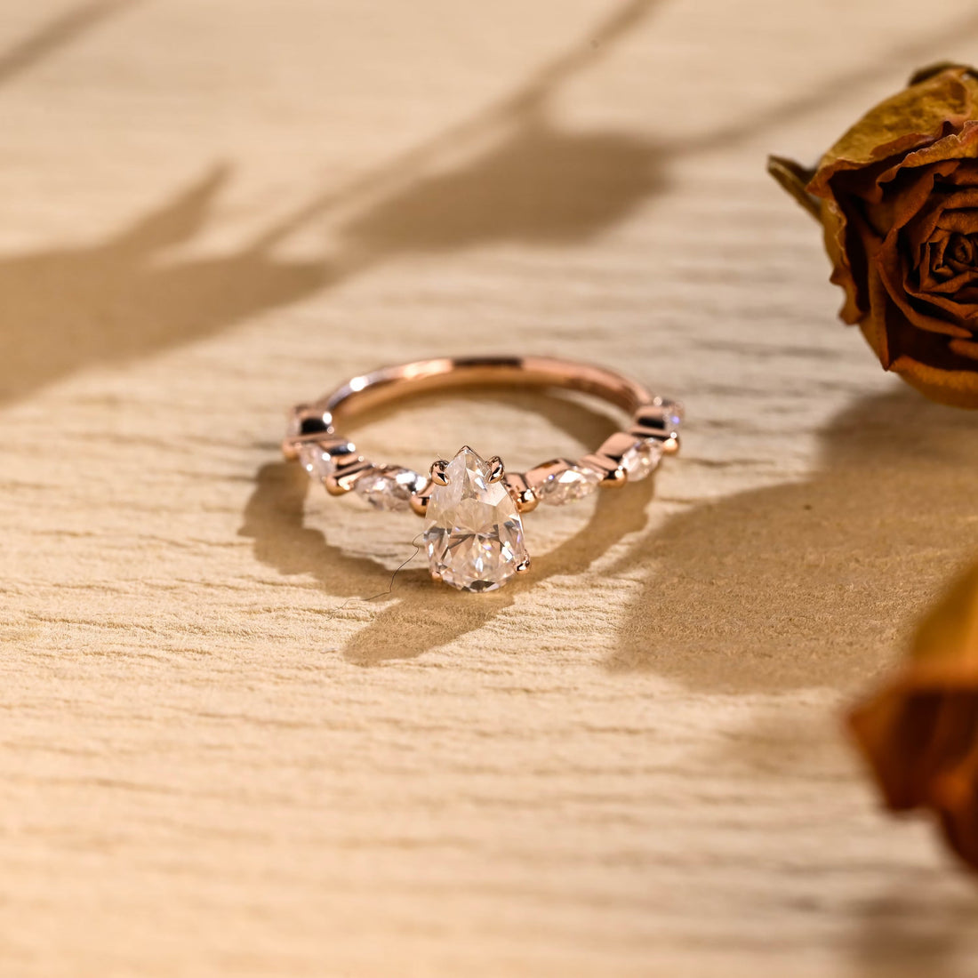 Pear cut moissanite engagement ring with marquise stones set lengthwise along both sides of a slim polished rose gold band