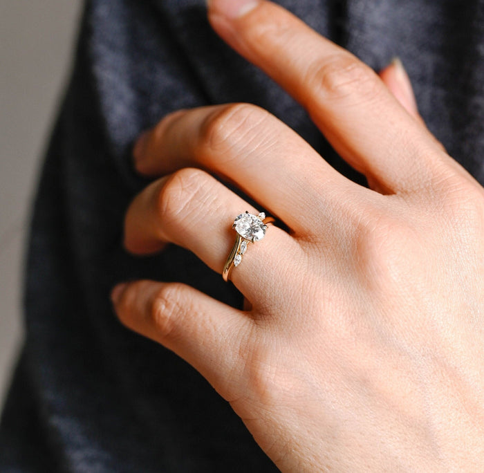 Oval moissanite bypass engagement ring with four claws and two marquise stones on each side of a sweeping yellow gold band, view 2