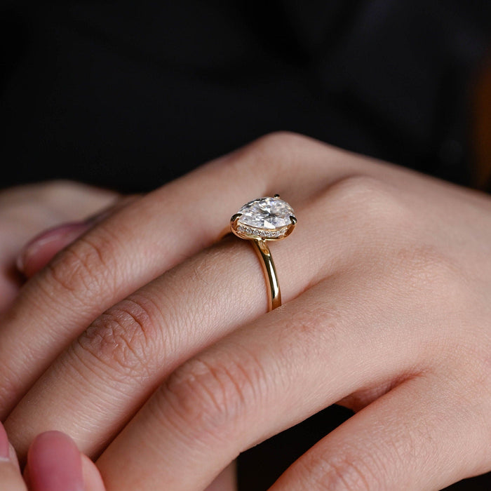 Pear shaped moissanite engagement ring held by three claws with a hidden halo beneath on a slim polished yellow gold band, view 2