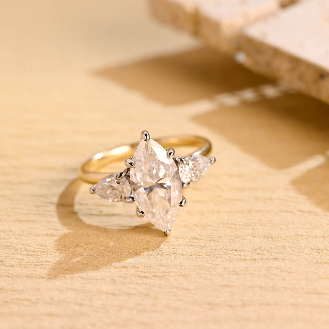 Marquise cut moissanite three stone engagement ring with pear side stones in a white gold setting on a yellow gold band
