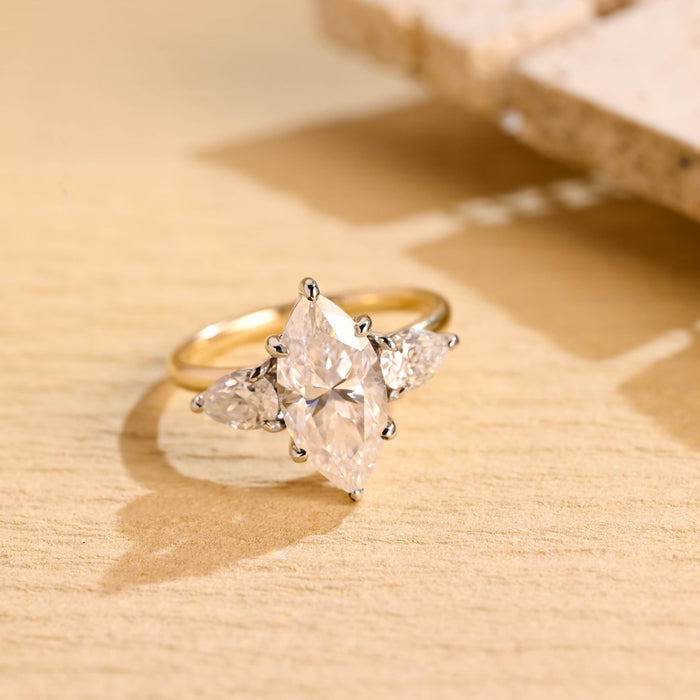 Marquise cut moissanite three stone engagement ring with pear side stones in a white gold setting on a yellow gold band