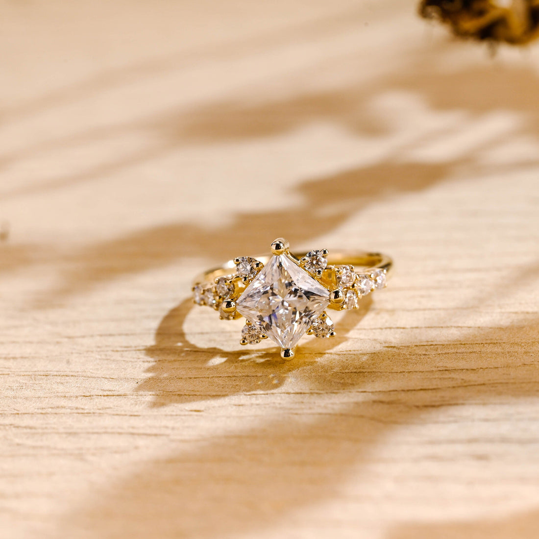 Princess cut moissanite kite set cluster engagement ring with round stones on the shoulders in yellow gold