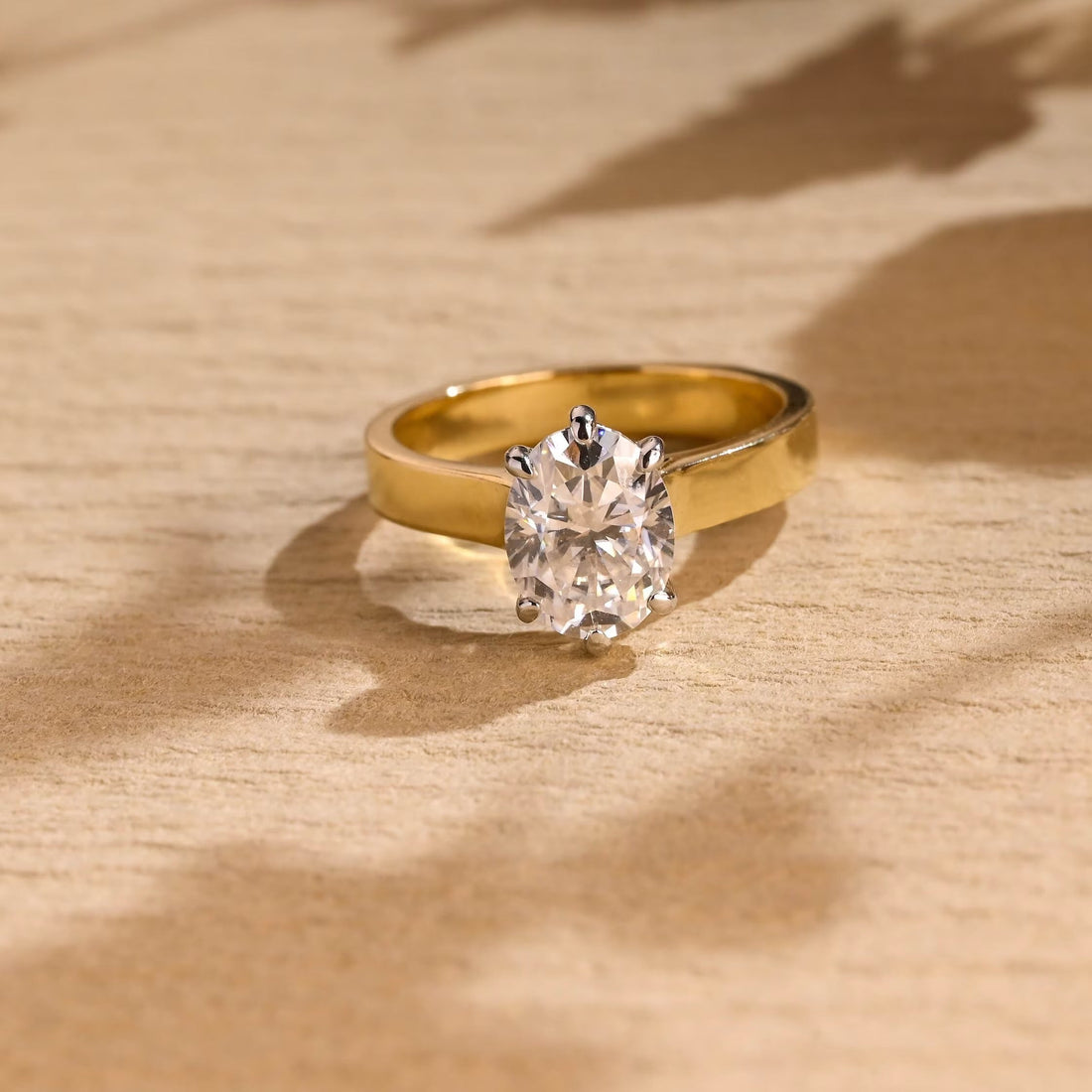 Oval moissanite six claw solitaire engagement ring on a wide flat polished yellow gold band with white gold claws