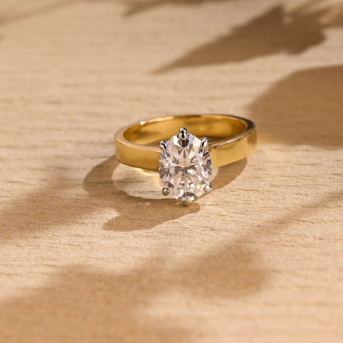 Oval moissanite six claw solitaire engagement ring on a wide flat polished yellow gold band with white gold claws