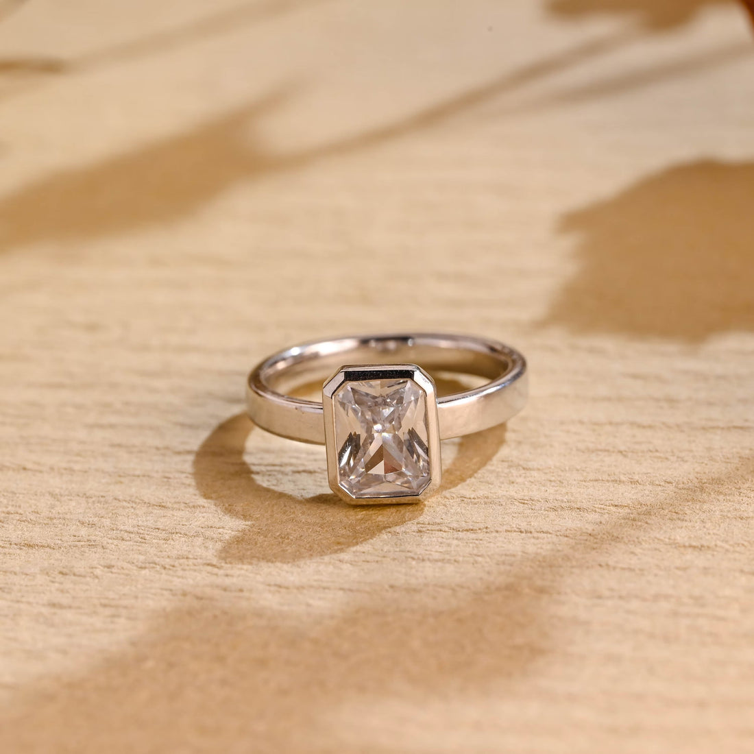 Radiant cut moissanite bezel set solitaire engagement ring on a wide flat polished white gold band