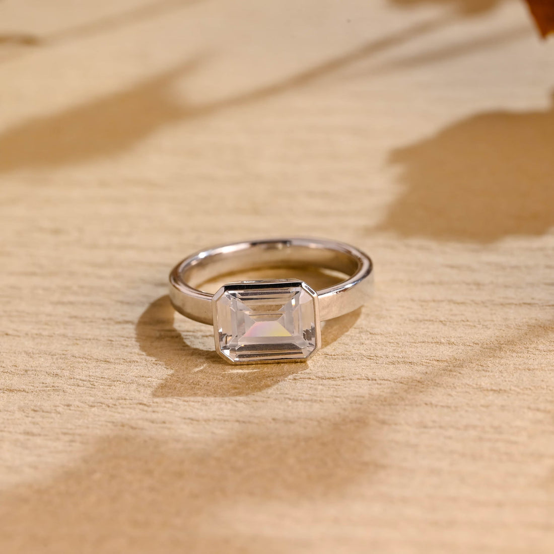 East west emerald cut moissanite bezel set solitaire engagement ring on a thick polished white gold band