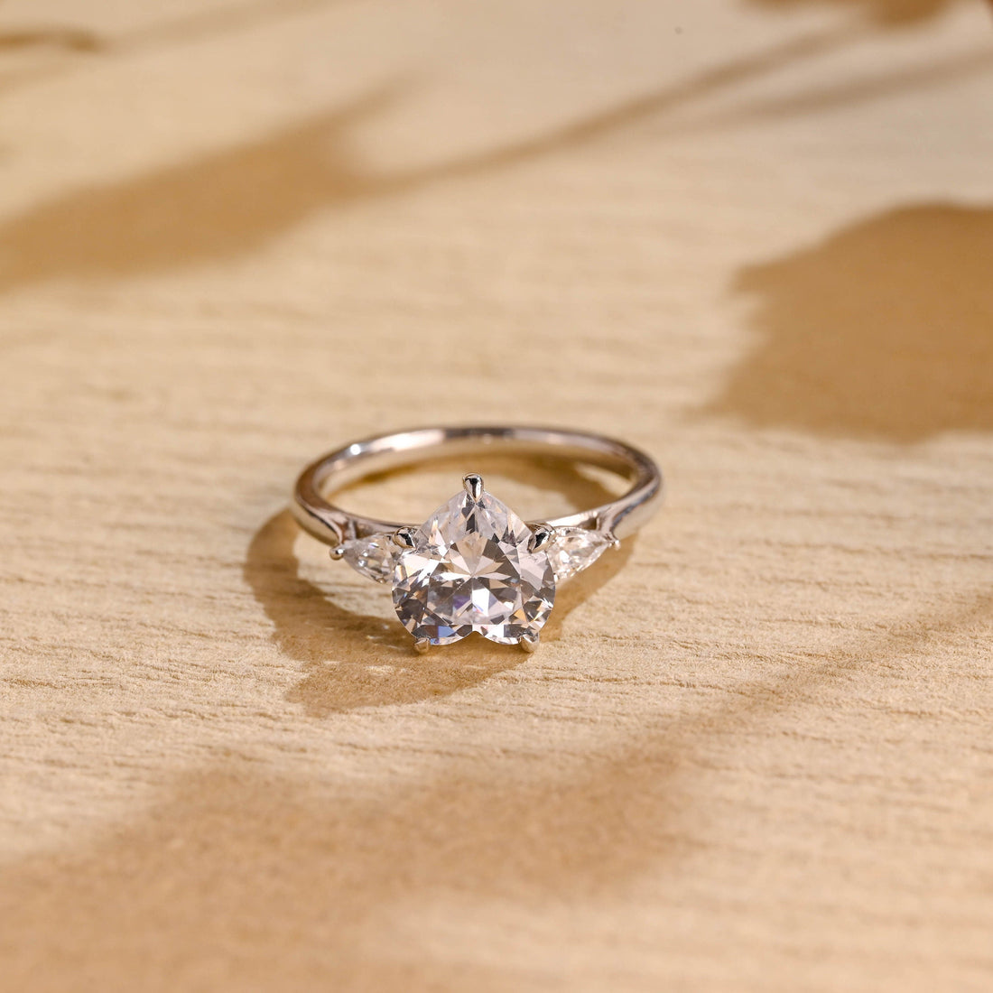 Heart cut moissanite three stone engagement ring with pear cut side stones on a polished white gold band