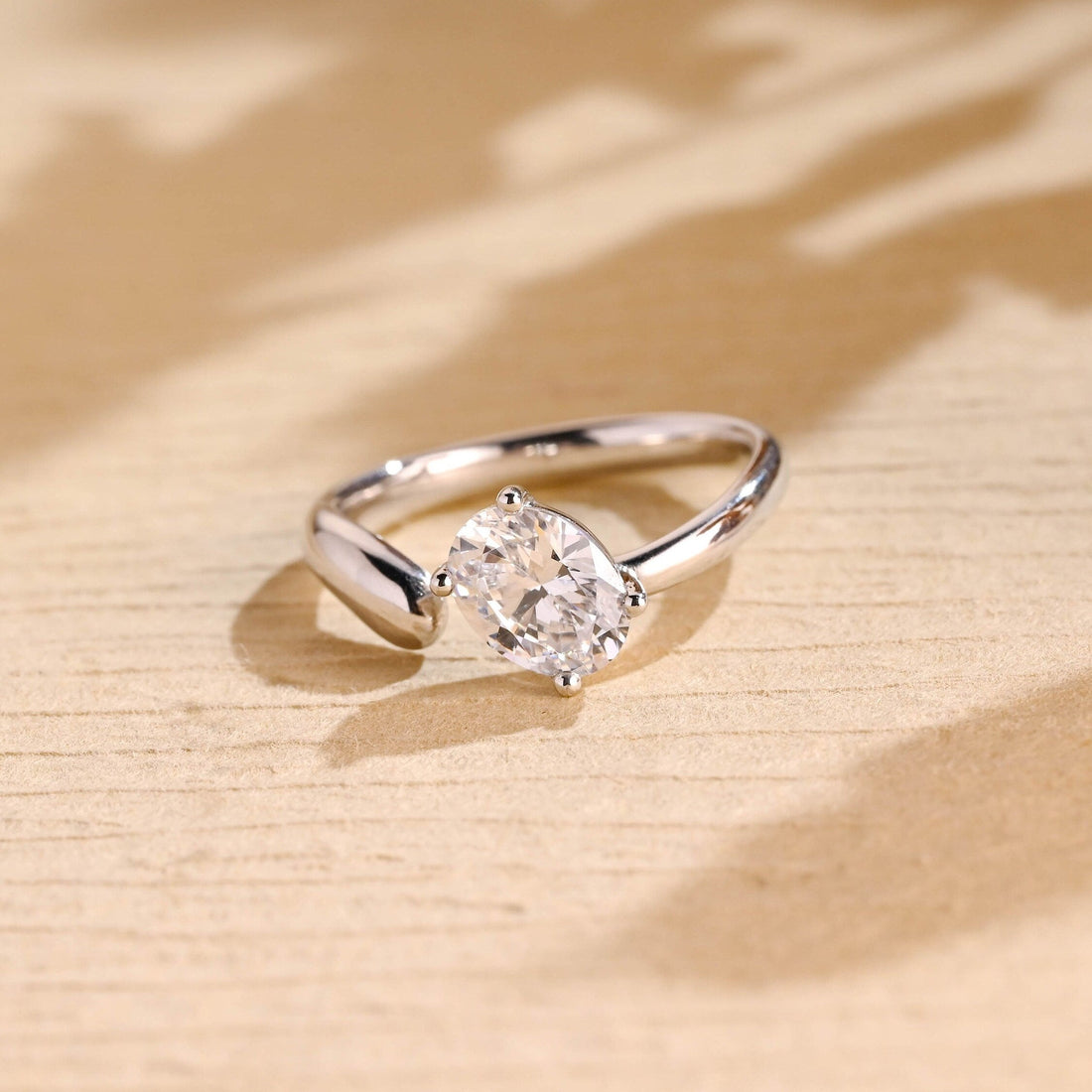 Oval moissanite open shank solitaire engagement ring with the stone tilted in four ball tipped claws on a sweeping polished white gold band