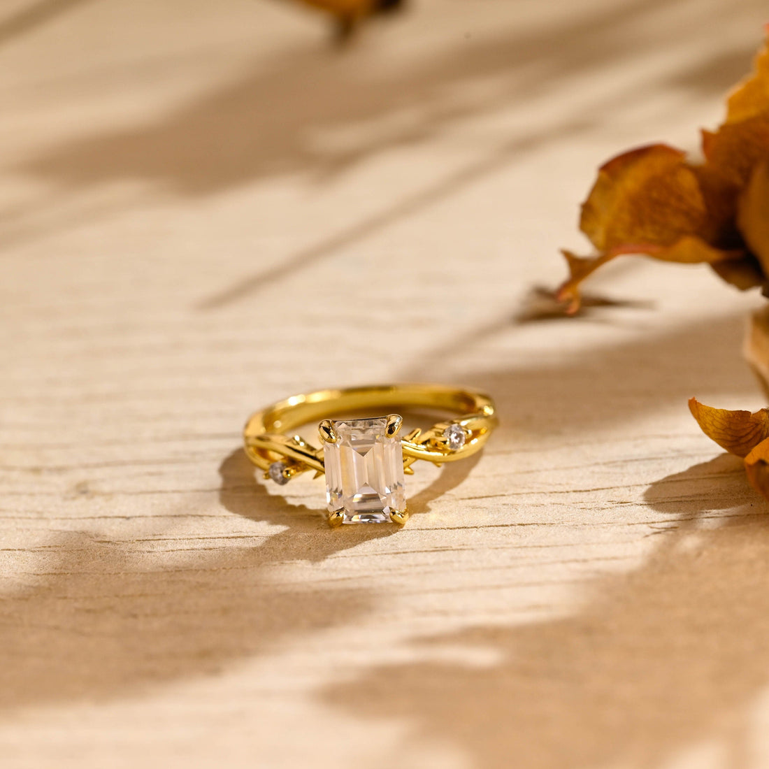 Emerald cut moissanite twig engagement ring with a crossing branch band, tiny thorns and a small stone on each side in yellow gold
