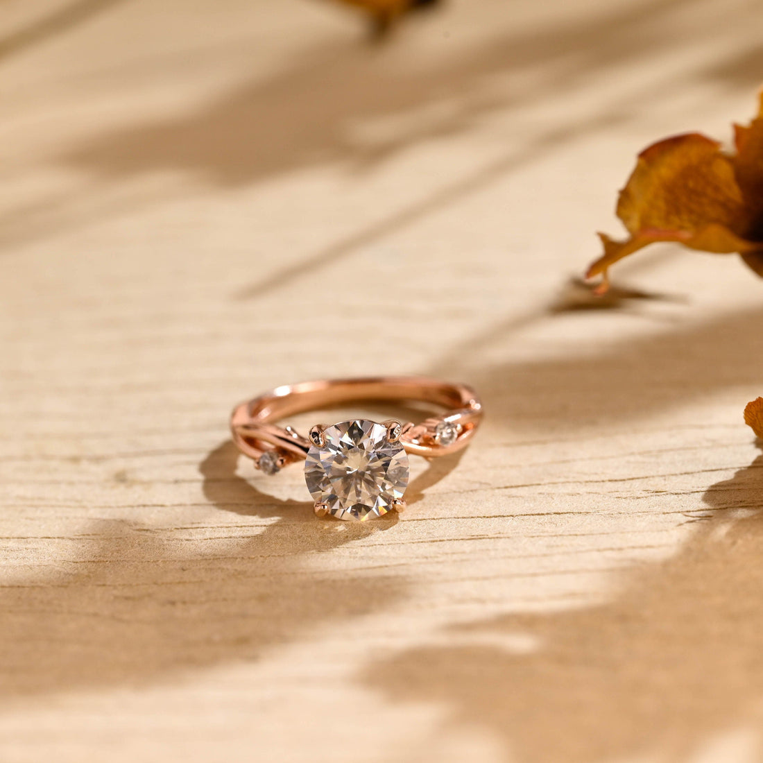 Round moissanite engagement ring with four claws on a twisted branch shaped rose gold band with a tiny round stone on each side of the centre stone