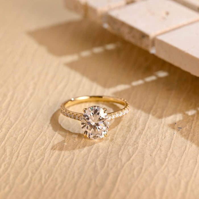 Oval moissanite hidden halo engagement ring with four claws and a slim pave set yellow gold band
