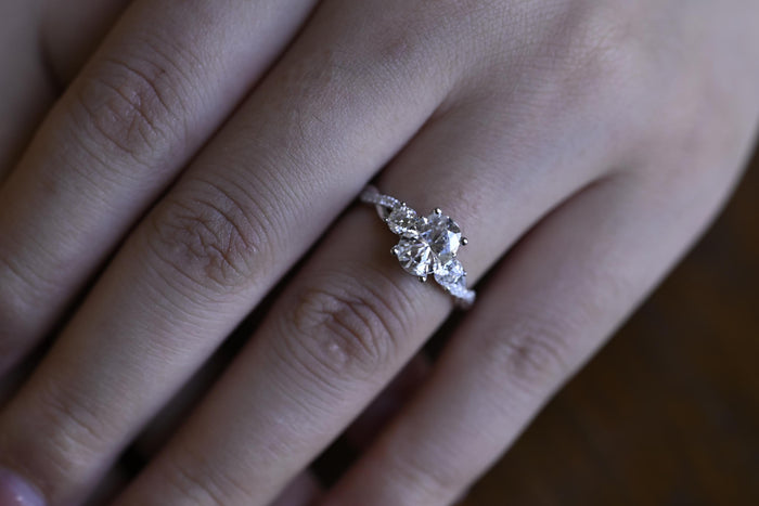 Oval moissanite three stone engagement ring with a round stone on each side and a twisted white gold band set with small round stones, view 2