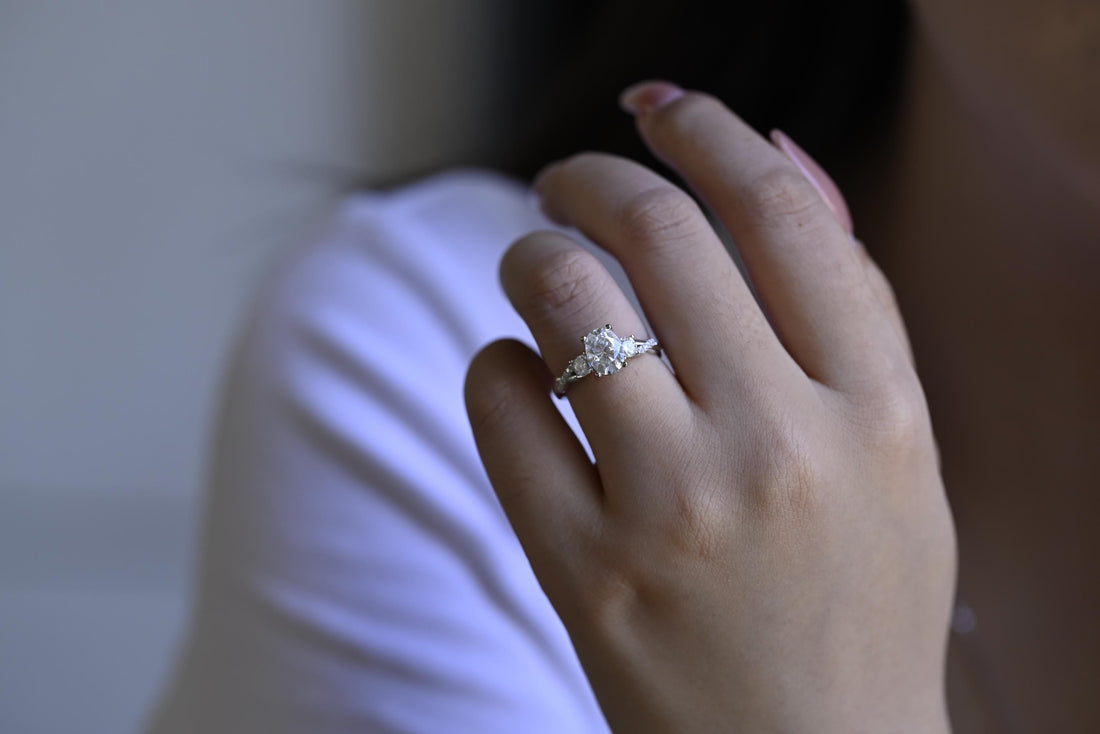 Oval moissanite three stone engagement ring with a round stone on each side and a twisted white gold band set with small round stones