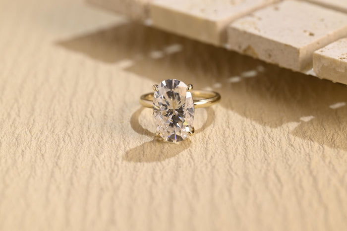 Oval moissanite solitaire engagement ring in four slim claws on a plain polished round yellow gold band