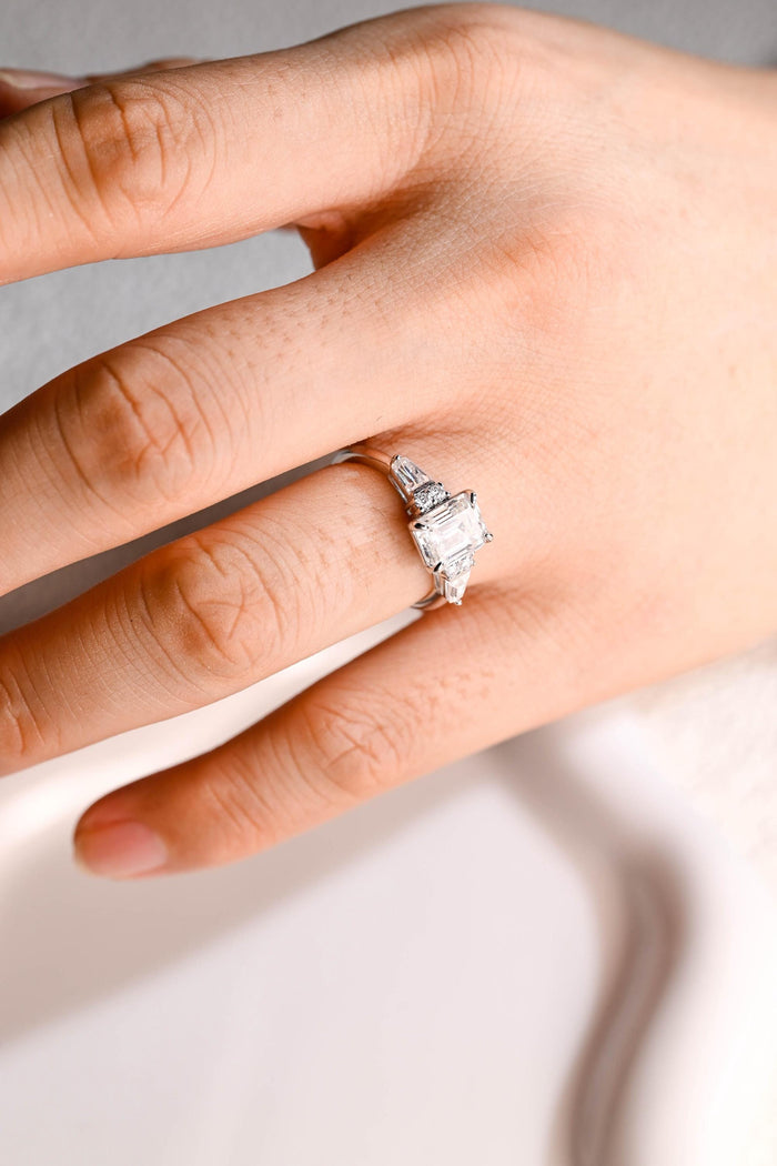 Emerald cut moissanite engagement ring with a pair of round stones and a tapered baguette on each side of a white gold band, view 2