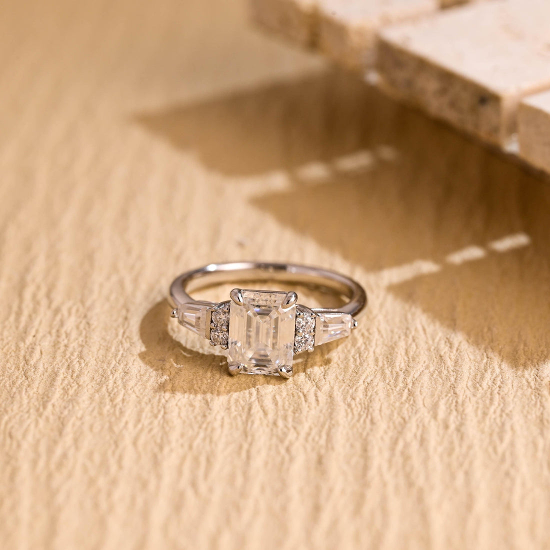 Emerald cut moissanite engagement ring with a pair of round stones and a tapered baguette on each side of a white gold band