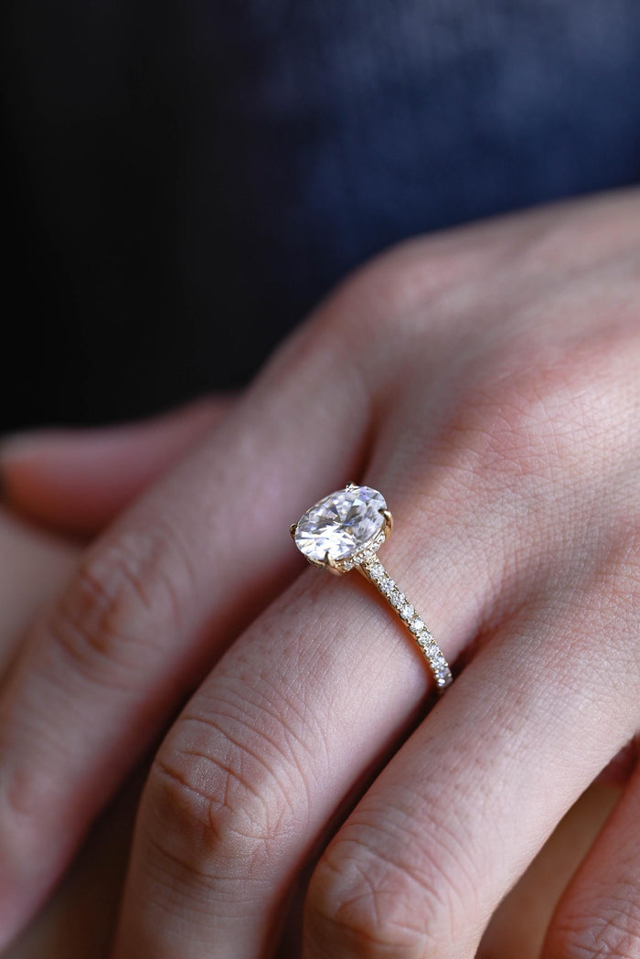 Oval moissanite hidden halo engagement ring with four claws and a slim pave set yellow gold band, view 2