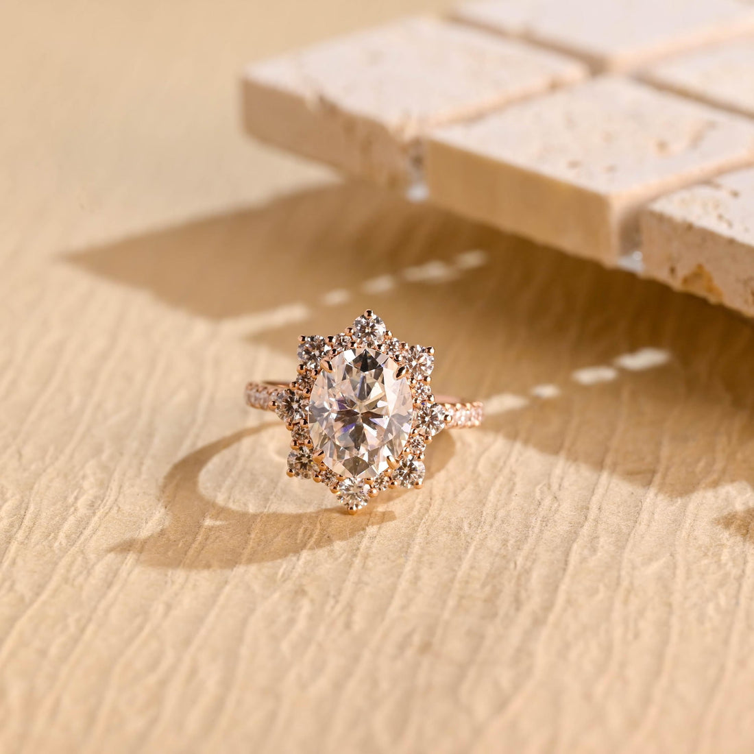 Oval moissanite floral halo engagement ring with a starburst of round stones around the centre stone and a pave set rose gold band