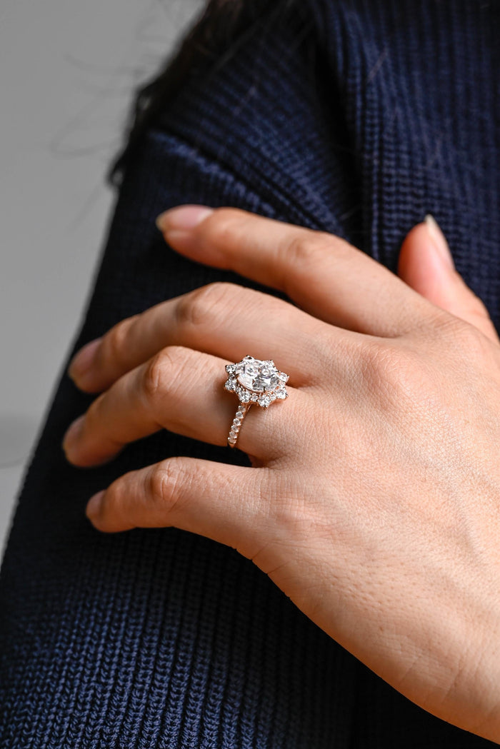 Oval moissanite floral halo engagement ring with a starburst of round stones around the centre stone and a pave set rose gold band, view 2