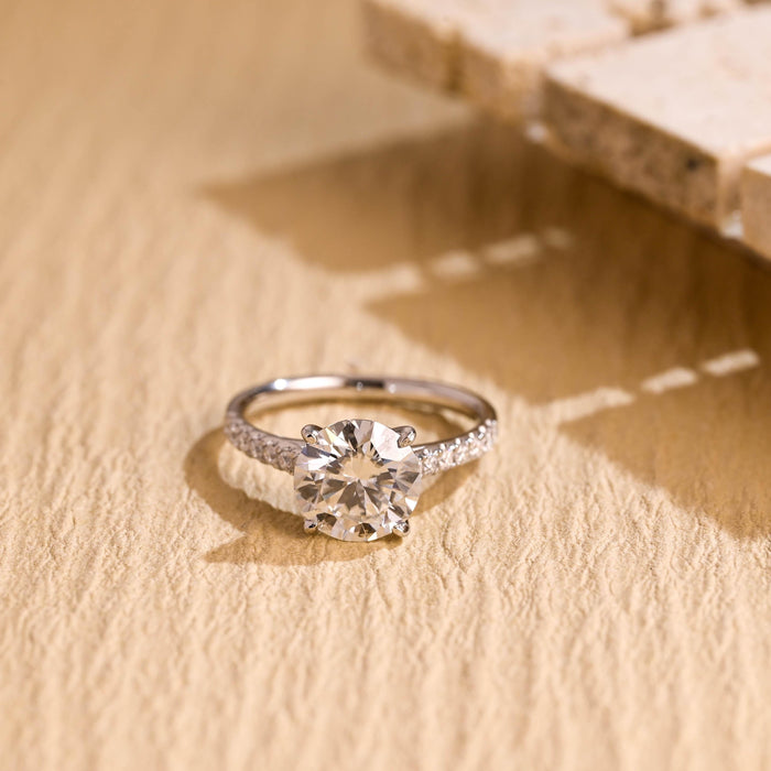 Round moissanite solitaire engagement ring in four slim claws on a fine white gold band pave set with tiny round stones along the shoulders