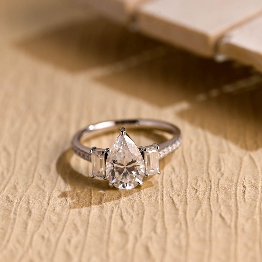 Pear cut moissanite three stone engagement ring with two baguette side stones and a pave set white gold band
