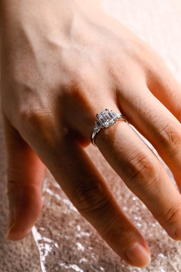 Emerald cut moissanite five stone engagement ring with baguette and trillion side stones on a slim white gold band, view 2