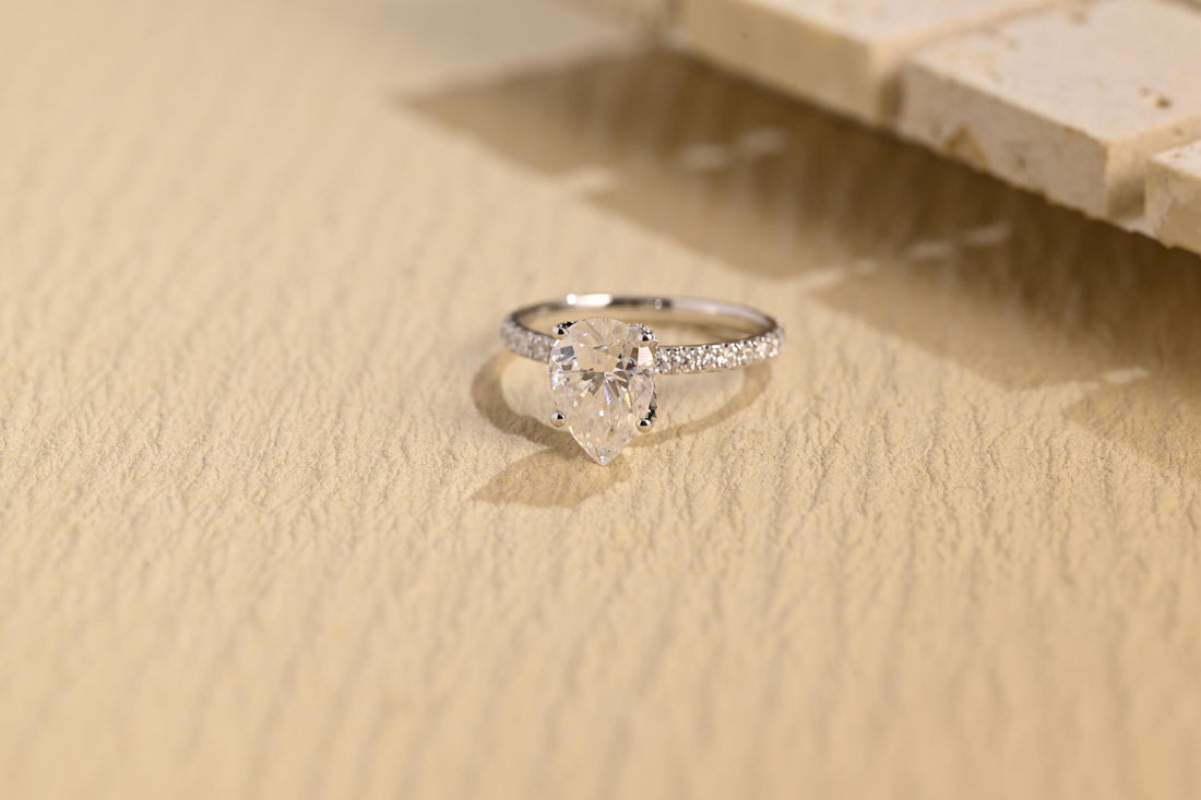 Pear shaped moissanite solitaire engagement ring in claws on a very slim white gold band pave set with tiny round stones