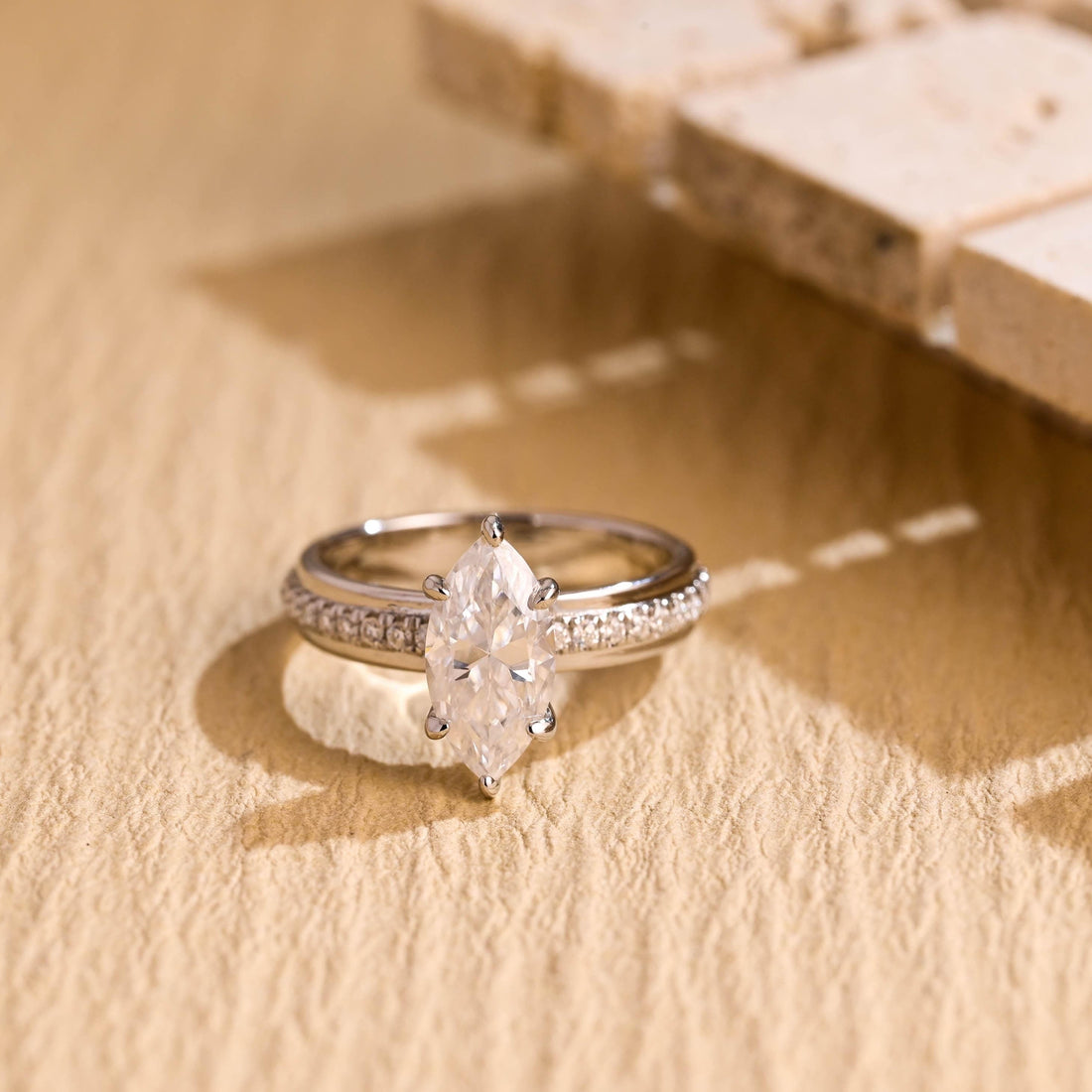 Marquise cut moissanite six claw solitaire ring on a white gold band with pave stones set into the sides