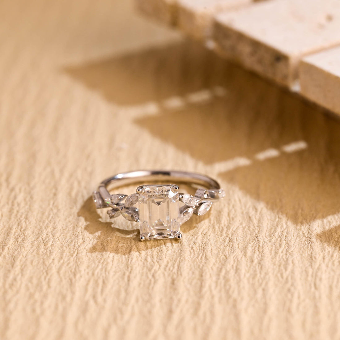 Emerald cut moissanite engagement ring with marquise leaf clusters on each shoulder of a slim white gold band