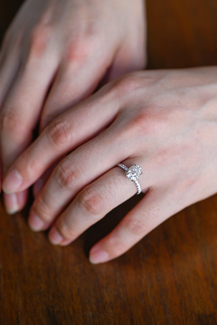 Oval moissanite solitaire engagement ring with four claws and a slim pave set white gold band, view 2