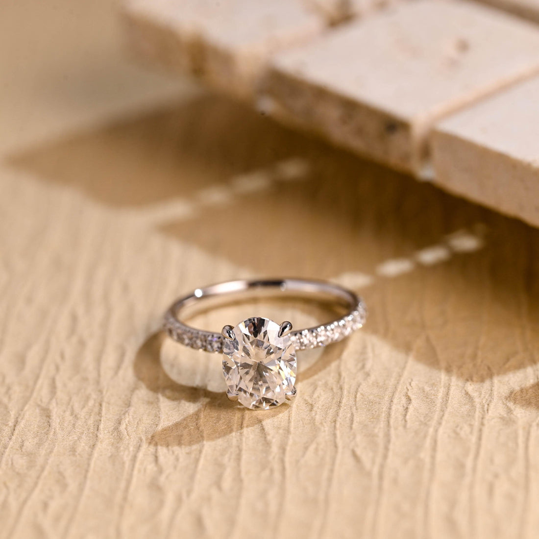 Oval moissanite solitaire engagement ring with four claws and a slim pave set white gold band