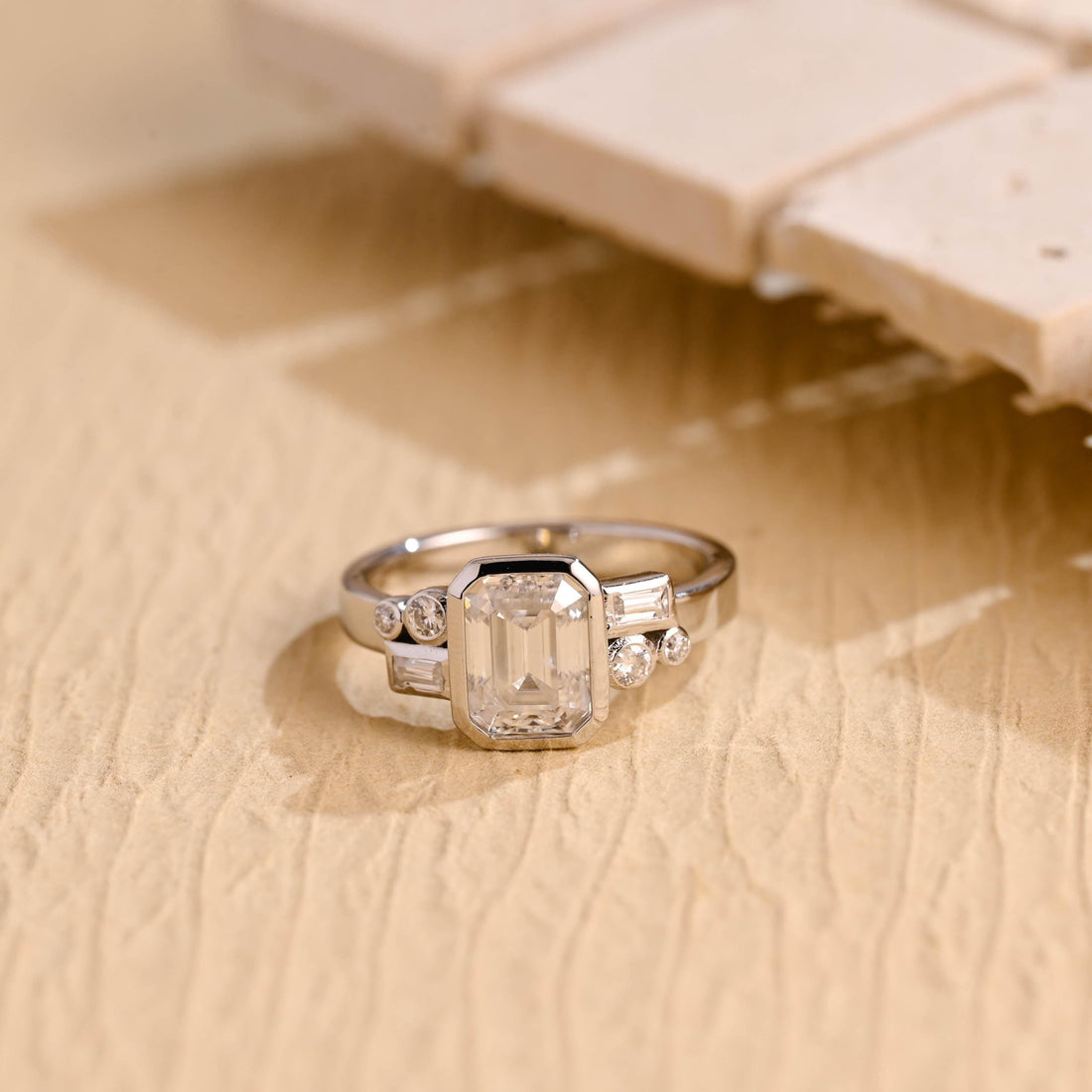 Emerald cut moissanite bezel engagement ring with baguette and round accent stones on a polished white gold band