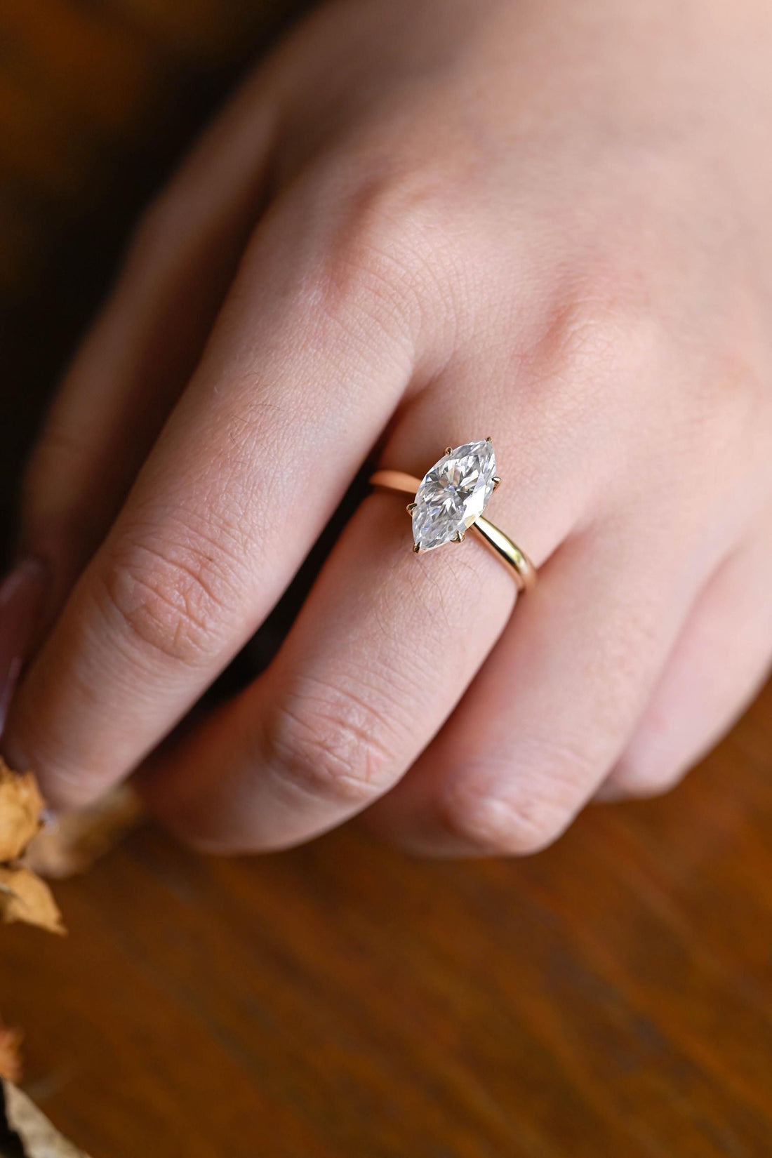 Marquise cut moissanite six claw tulip style solitaire engagement ring worn on a hand with a slim yellow gold band