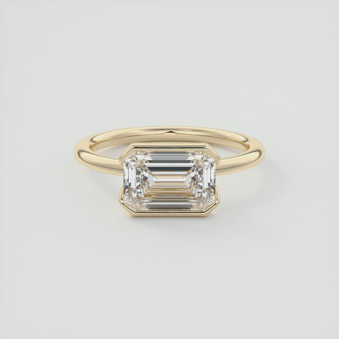 Emerald cut moissanite east west half bezel engagement ring in yellow gold