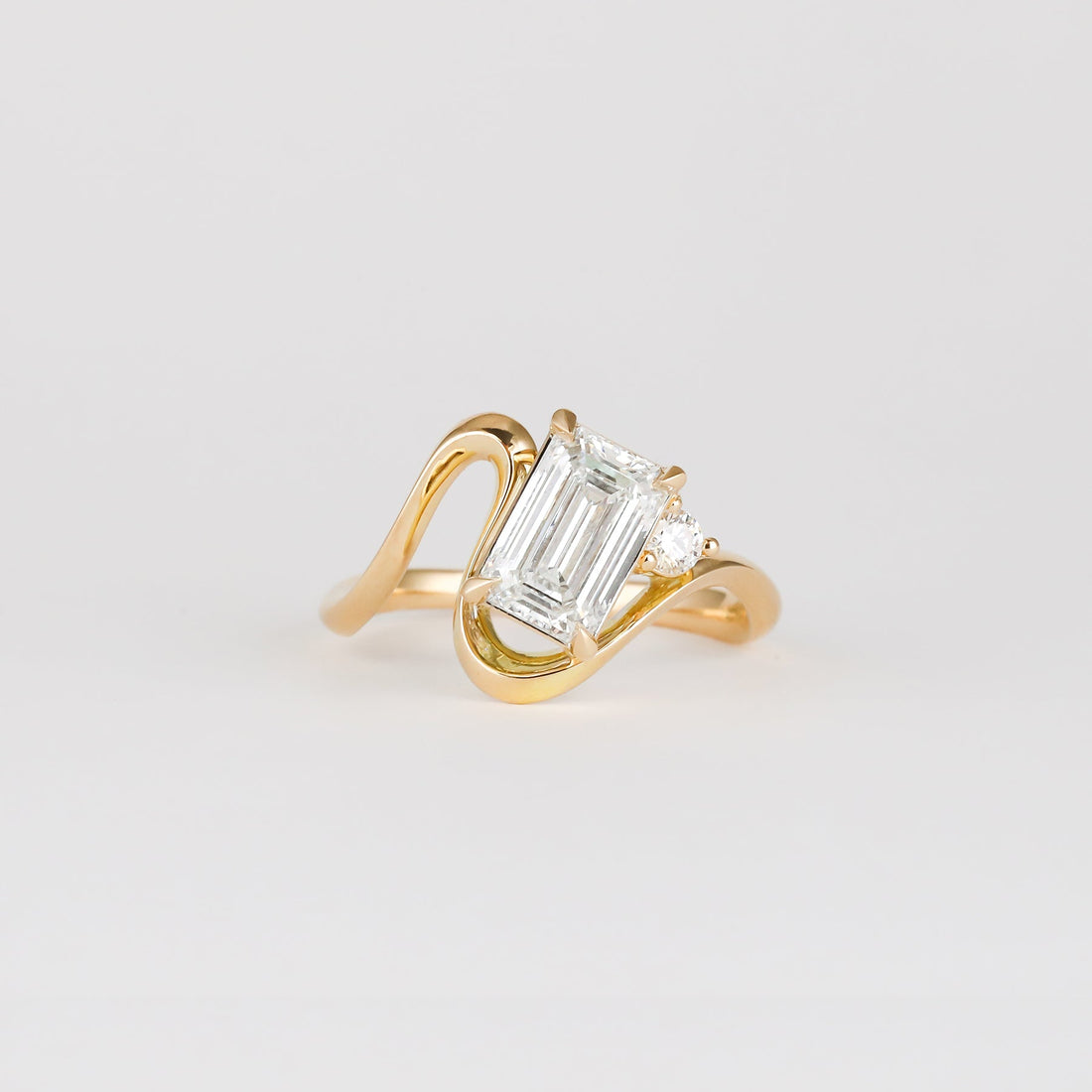Emerald cut lab grown diamond ring on a sculpted curved band in yellow gold
