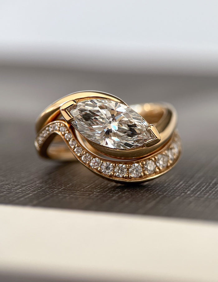 Close-up of east-west marquise lab grown diamond V-tip swirl ring nested with graduated stone wave band