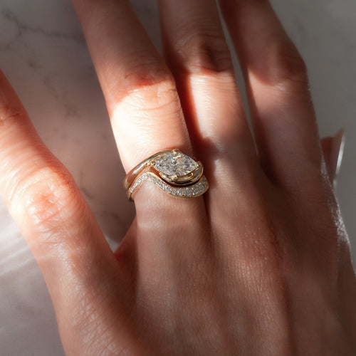 East-west marquise moissanite four-prong swirl bridal set in yellow gold on the hand in sunlight