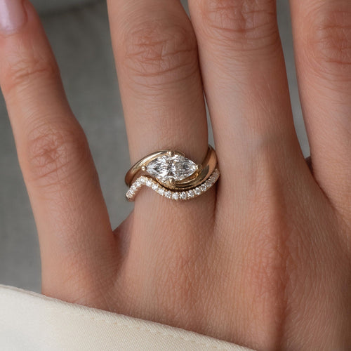 East-west marquise moissanite four-prong swirl ring with thin pave wave band in yellow gold, close-up on the hand