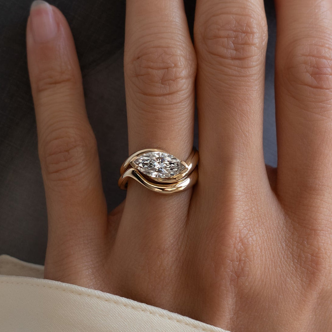 East-west marquise moissanite swirl bridal set with plain wave band in yellow gold on the hand