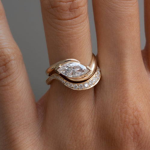 East-west marquise moissanite in V-tip prongs on a swirl bypass ring with graduated pave band, worn on the hand