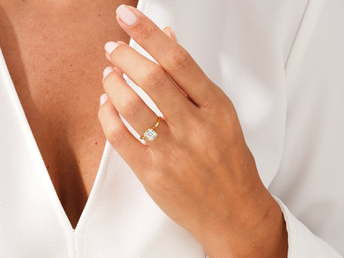 Asscher lab grown diamond bezel engagement ring in yellow gold worn on the hand against a white blouse